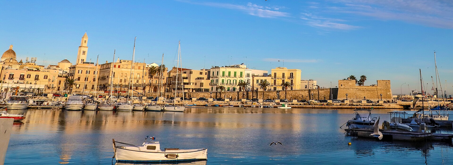 Bari's old harbor, waterfront buildings and cathedral bell tower beneath a blue sky