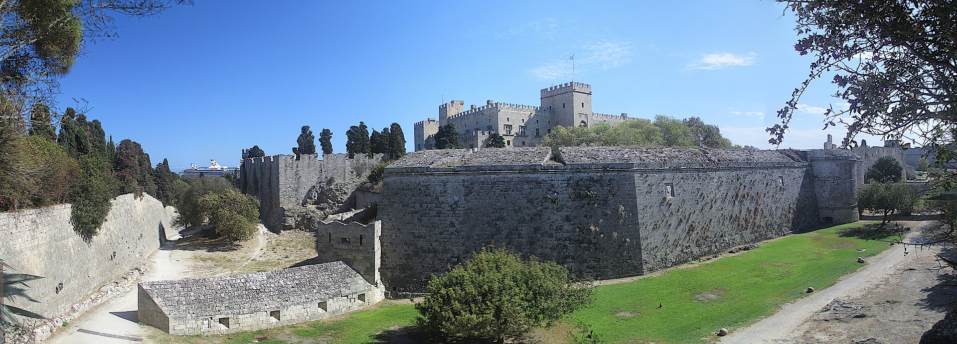 Medieval stone walls and towers surrounding the Old Town of Rhodes beneath a blue sky