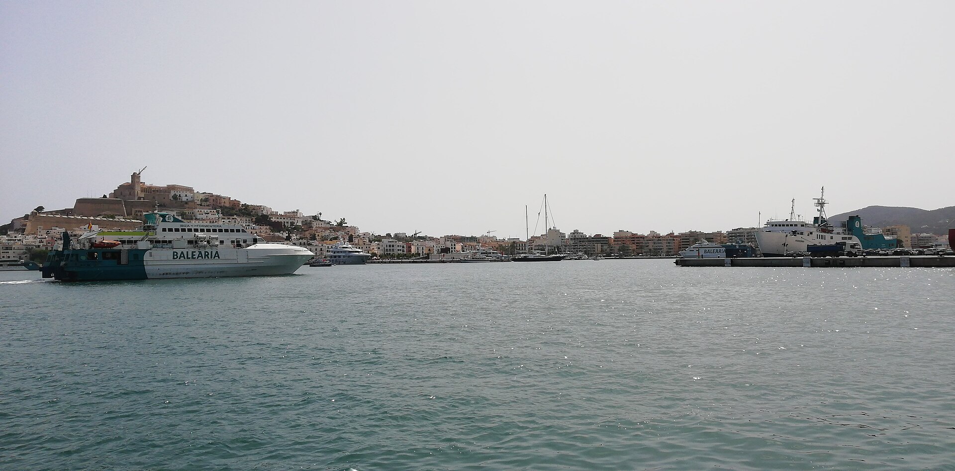 Passenger vessels crossing Ibiza harbor with Dalt Vila above the waterfront